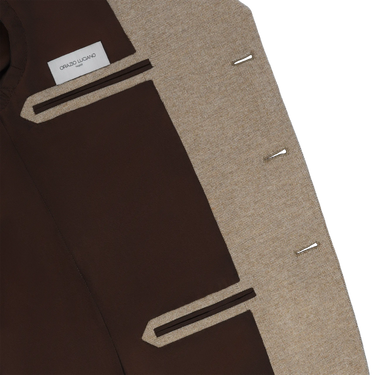 Interior view of Orazio Luciano beige wool jacket featuring brown lining and branded label, showcasing luxury finish and structure.