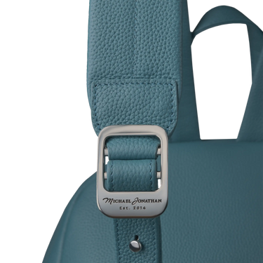 Close-up of Michael Jonathan branding on metal buckle of Classic Backpack in Baltic Blue, highlighting craftsmanship and luxury detail.
